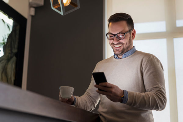 Avtnet Soluciones TIC Hombre sonriendo mientras revisa su teléfono móvil y sostiene una taza de café.